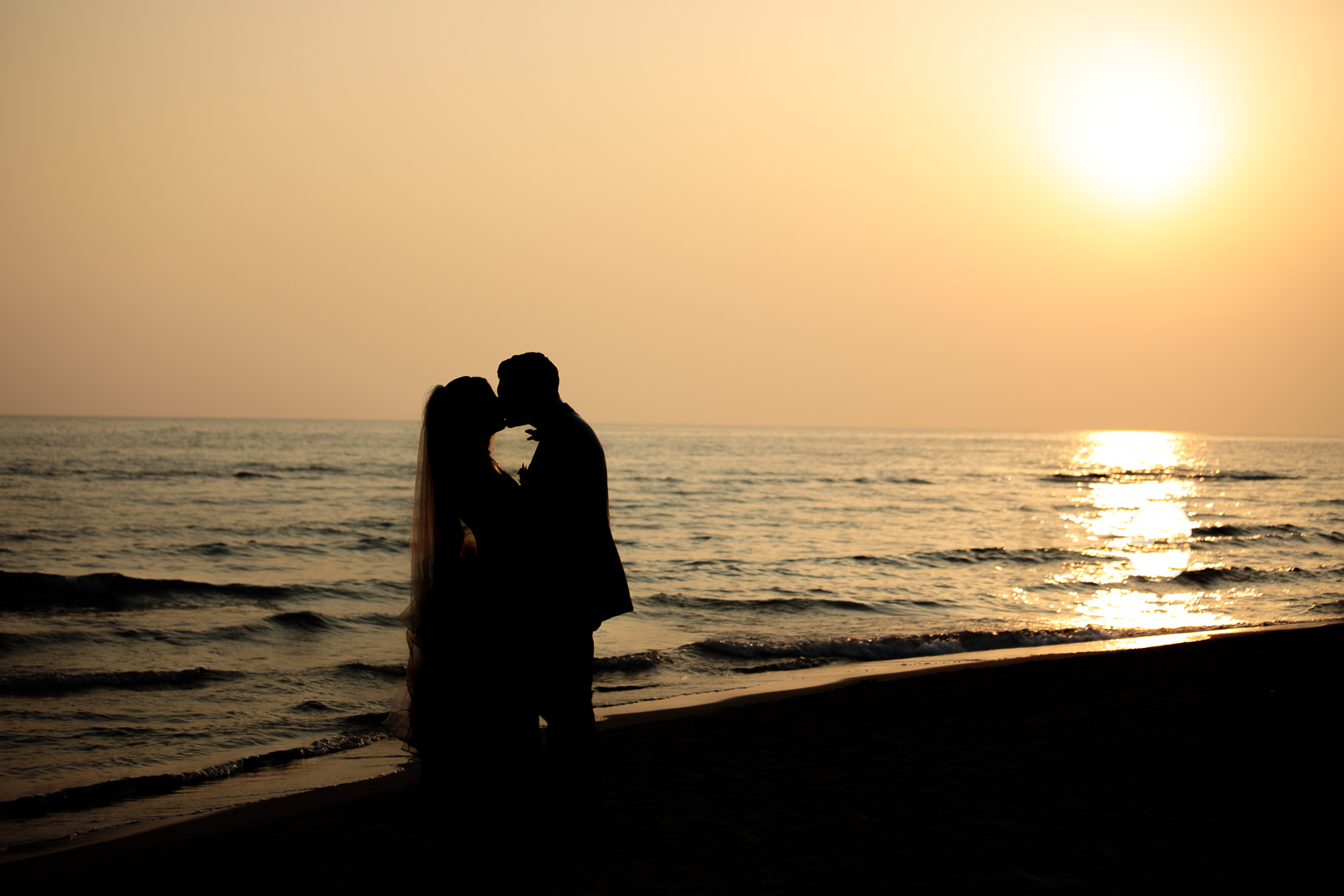 Sposi si baciano in spiaggia al tramonto - Fotografo matrimonio Roma prezzi